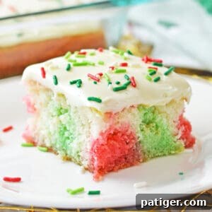 Christmas poke cake with pockets of red and green color throughout a fluffy white sheet cake and vanilla frosting with red and green sprinkles.