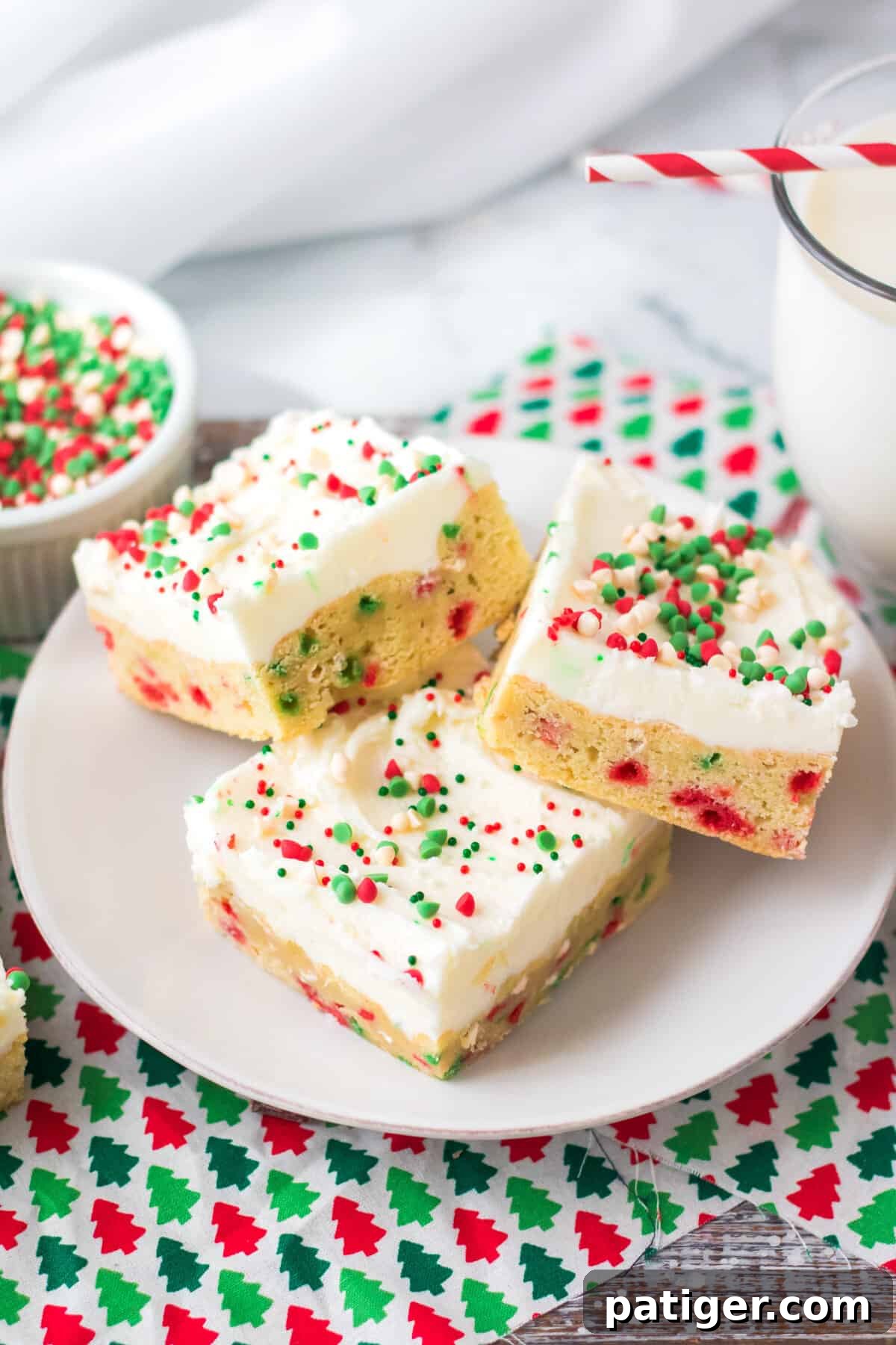 Frosted sugar cookie bars with Christmas sprinkles on white plate.