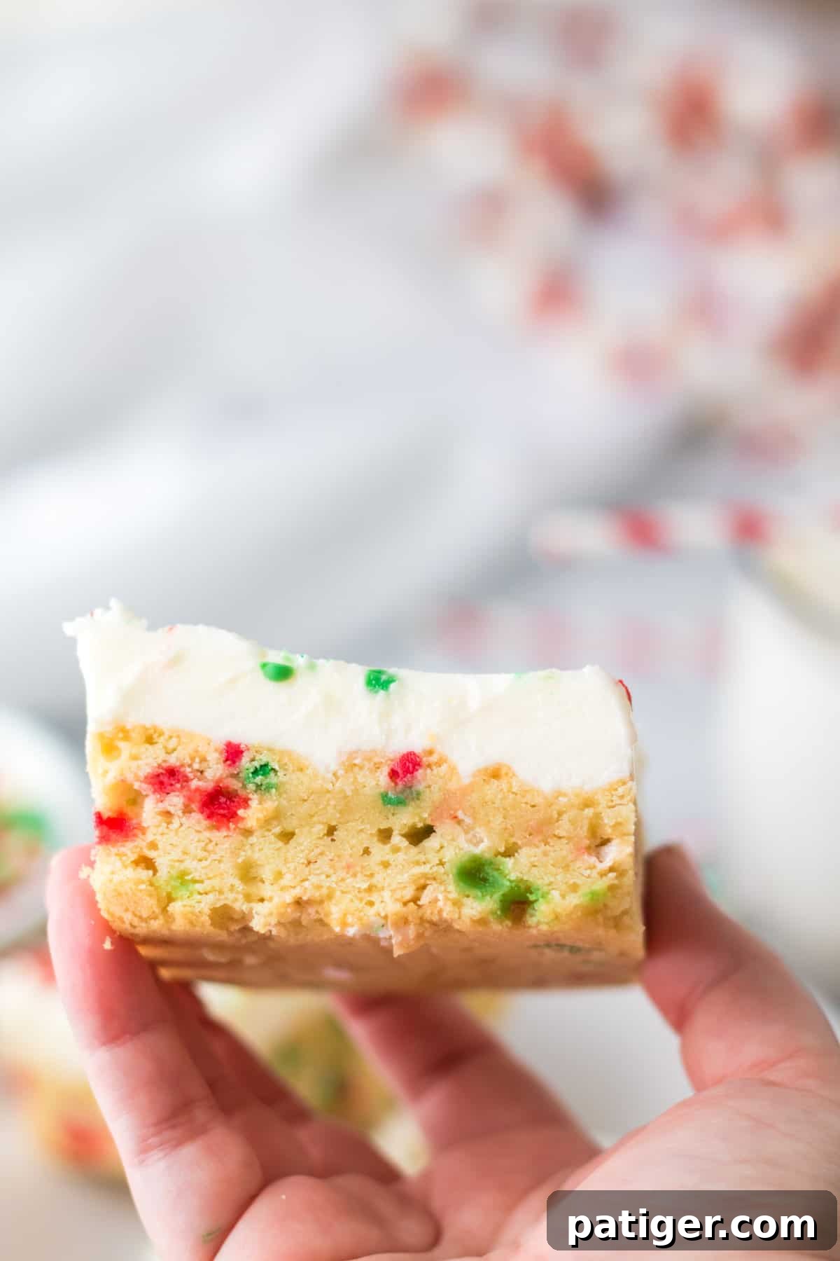 Hand holding thick and chewy frosted cookie bar with vanilla icing and christmas sprinkles.