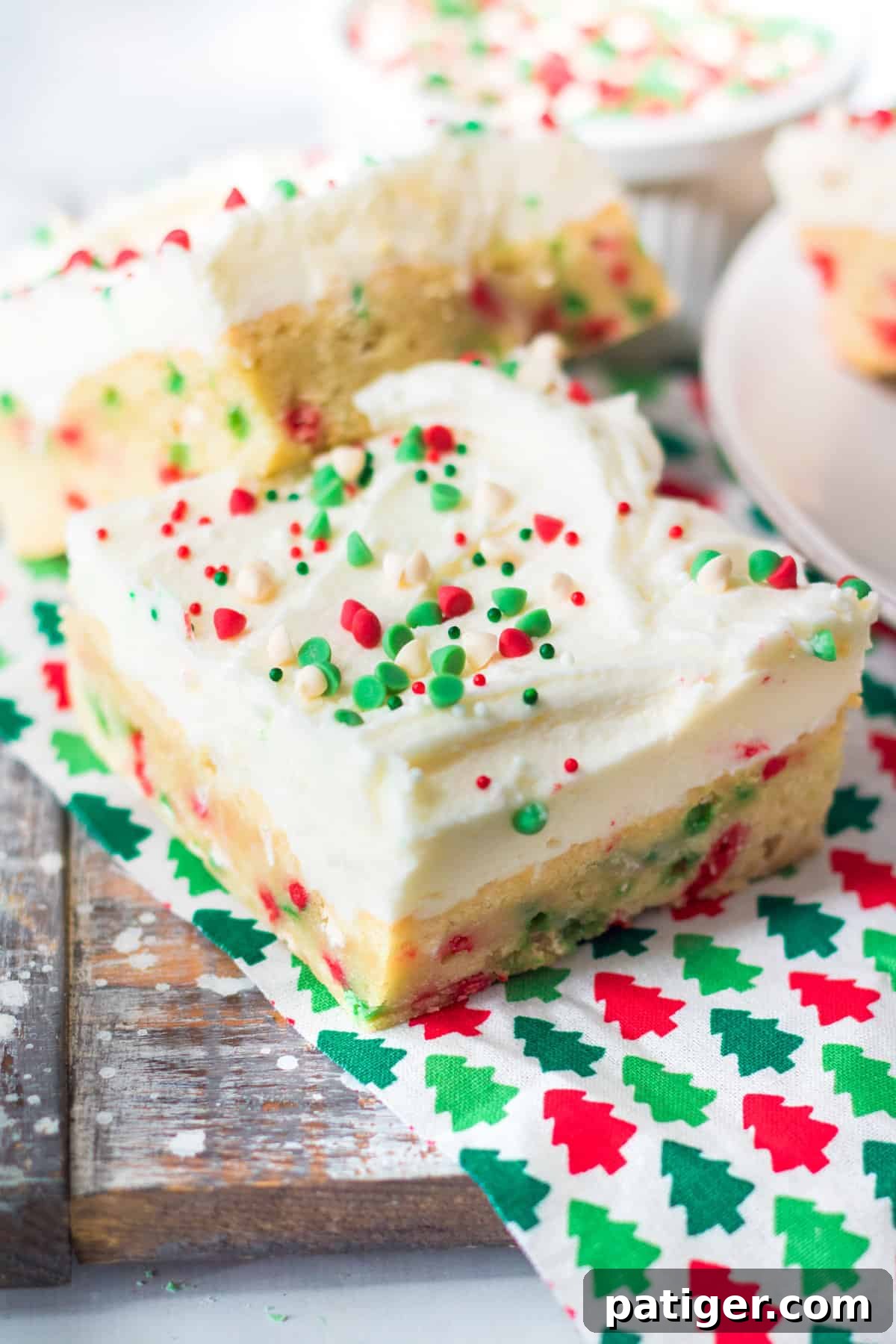 Sugar cookie bars with vanilla frosting and Christmas sprinkles on a holiday napkin.