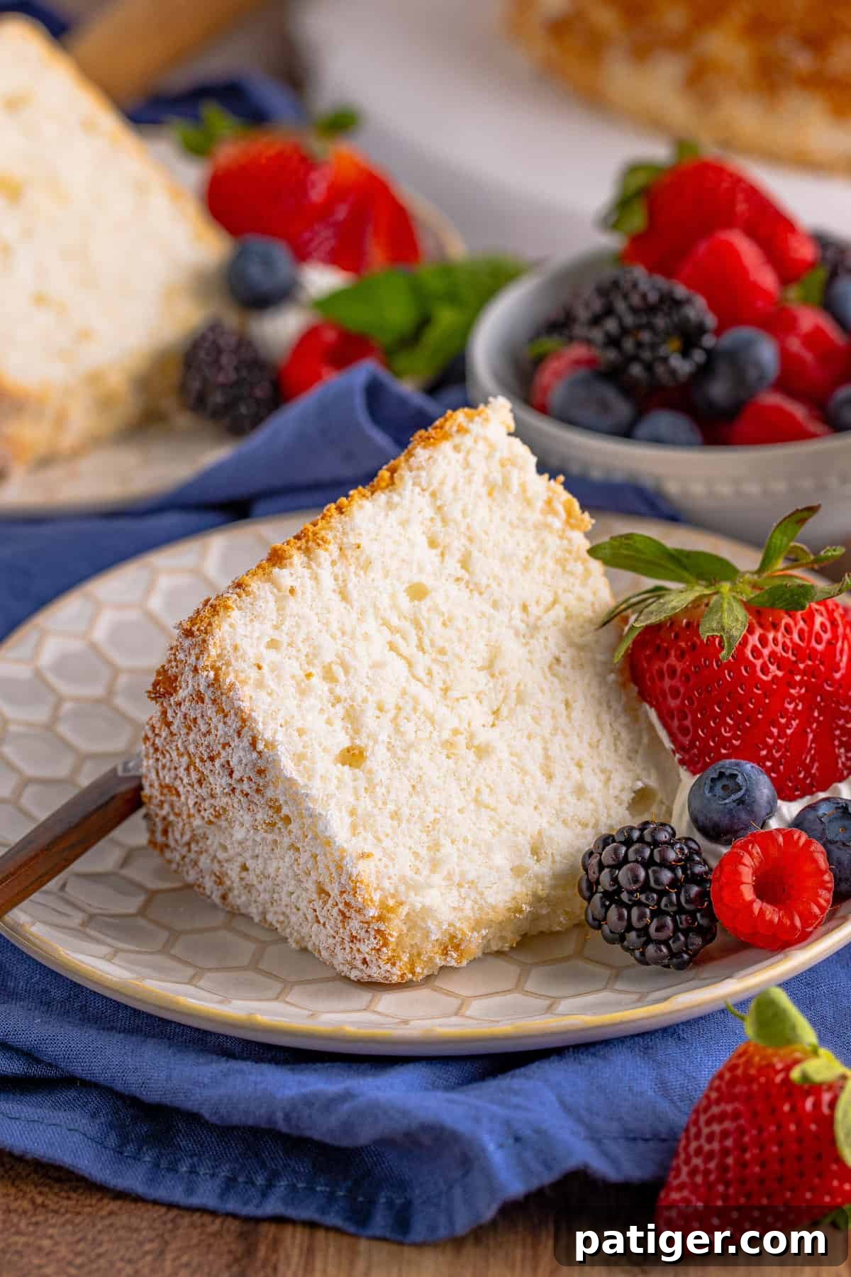 Feather-Light Angel Food Dream 2 A perfectly sliced piece of angel food cake served on a white plate with fresh, vibrant berries, highlighting its light and airy texture.