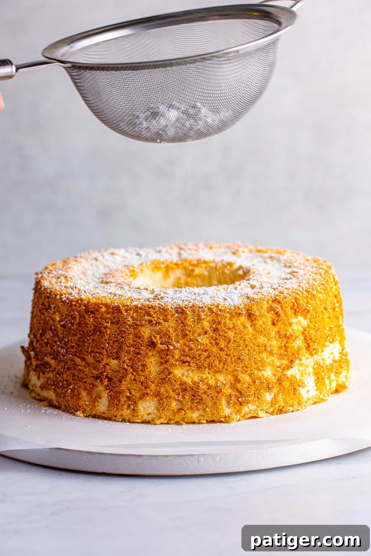 Feather-Light Angel Food Dream 12 Confectioners' sugar being delicately sifted over the top of a cooled homemade angel food cake, adding a final touch of elegance before serving.