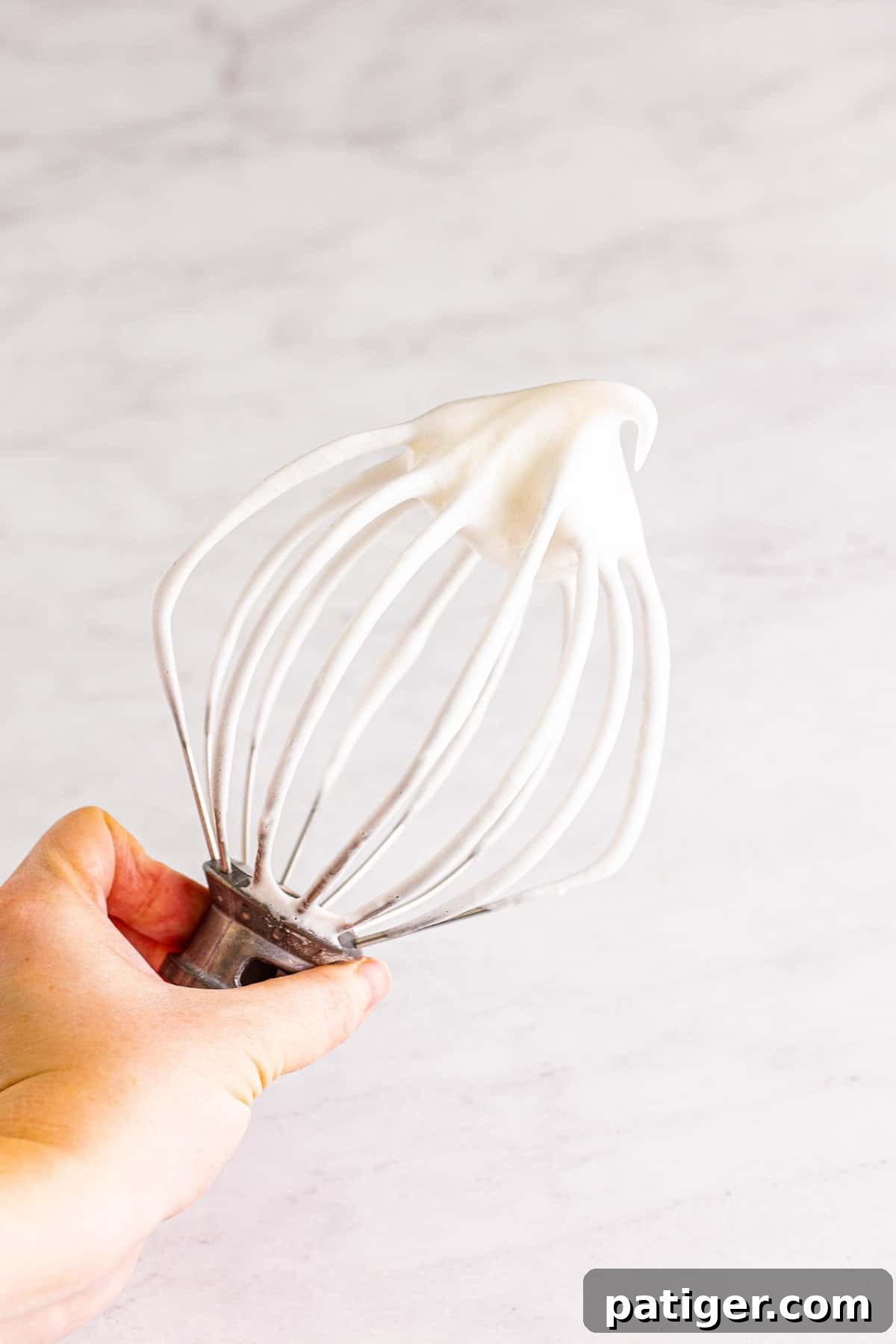 Feather-Light Angel Food Dream 7 Close-up of fluffy egg whites whipped to soft peaks on a stand mixer's whisk attachment, illustrating the ideal consistency for angel food cake batter.