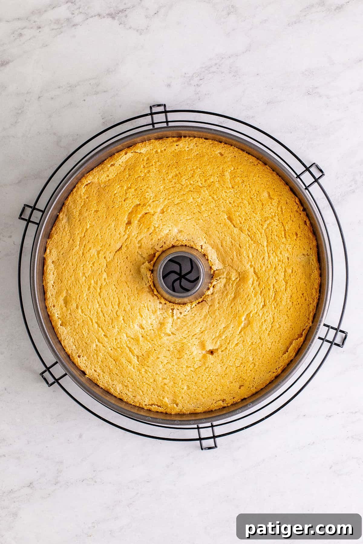 Feather-Light Angel Food Dream 10 A freshly baked, golden-brown homemade angel food cake cooling in its tube pan on a round wire rack, showcasing its perfect rise.