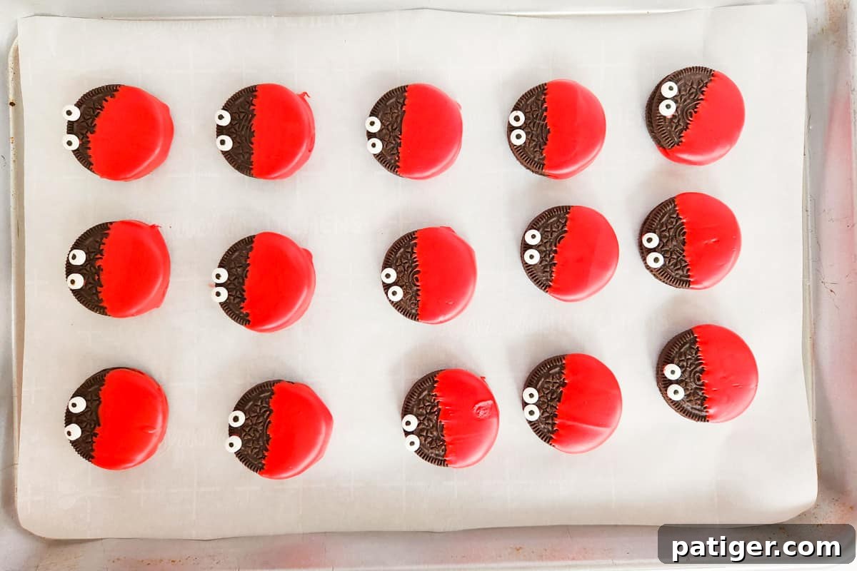 Dipped oreos with candy eyeballs on parchment-lined baking sheet.
