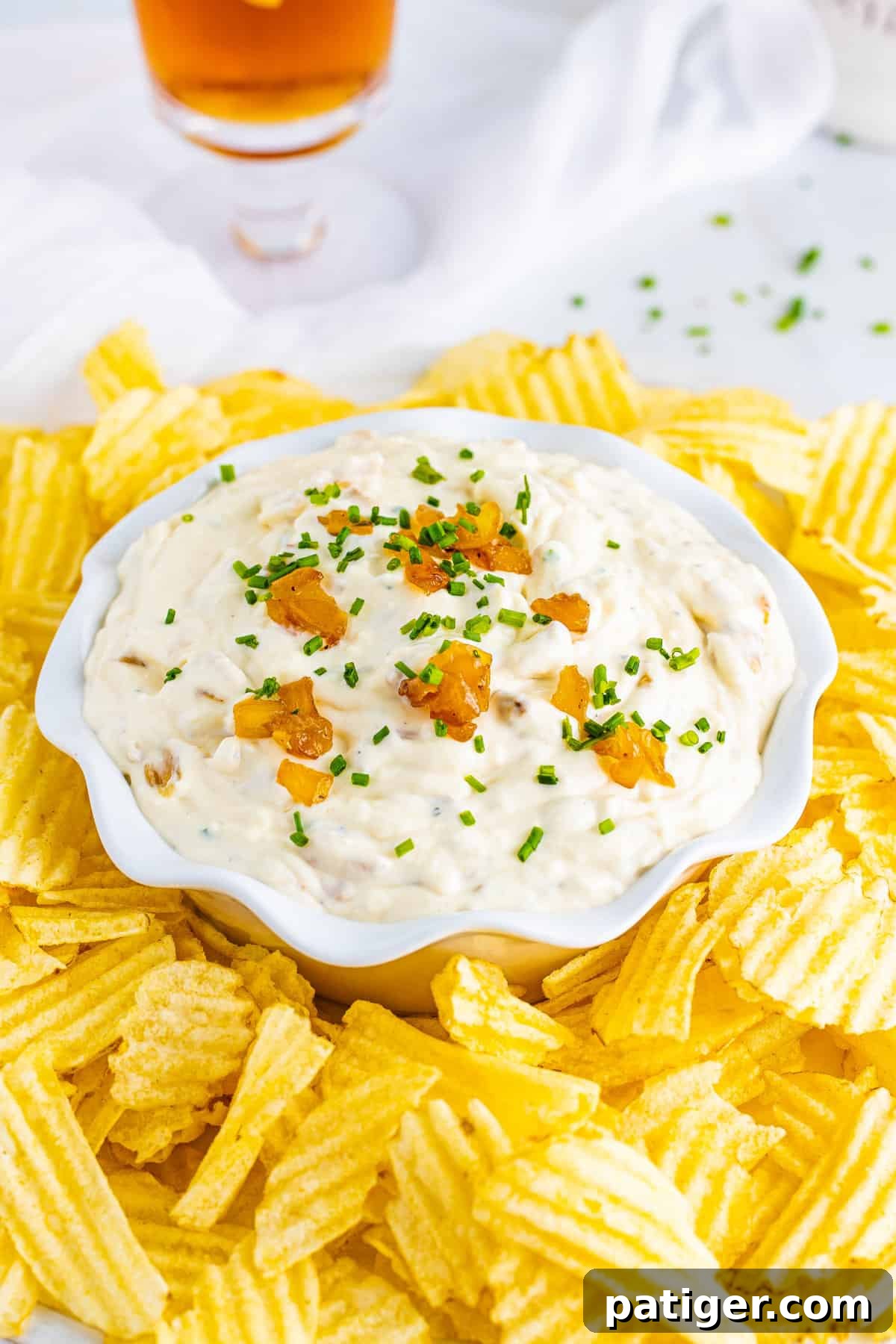 French onion dip garnished with chives in a bowl surrounded by crispy potato chips.