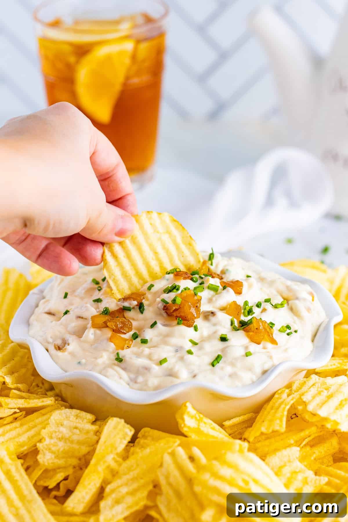 Hand dipping a potato chip in a bowl of French onion dip.