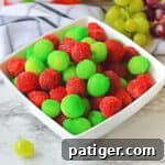 Candied grapes made with red and green jello powder in a white bowl.