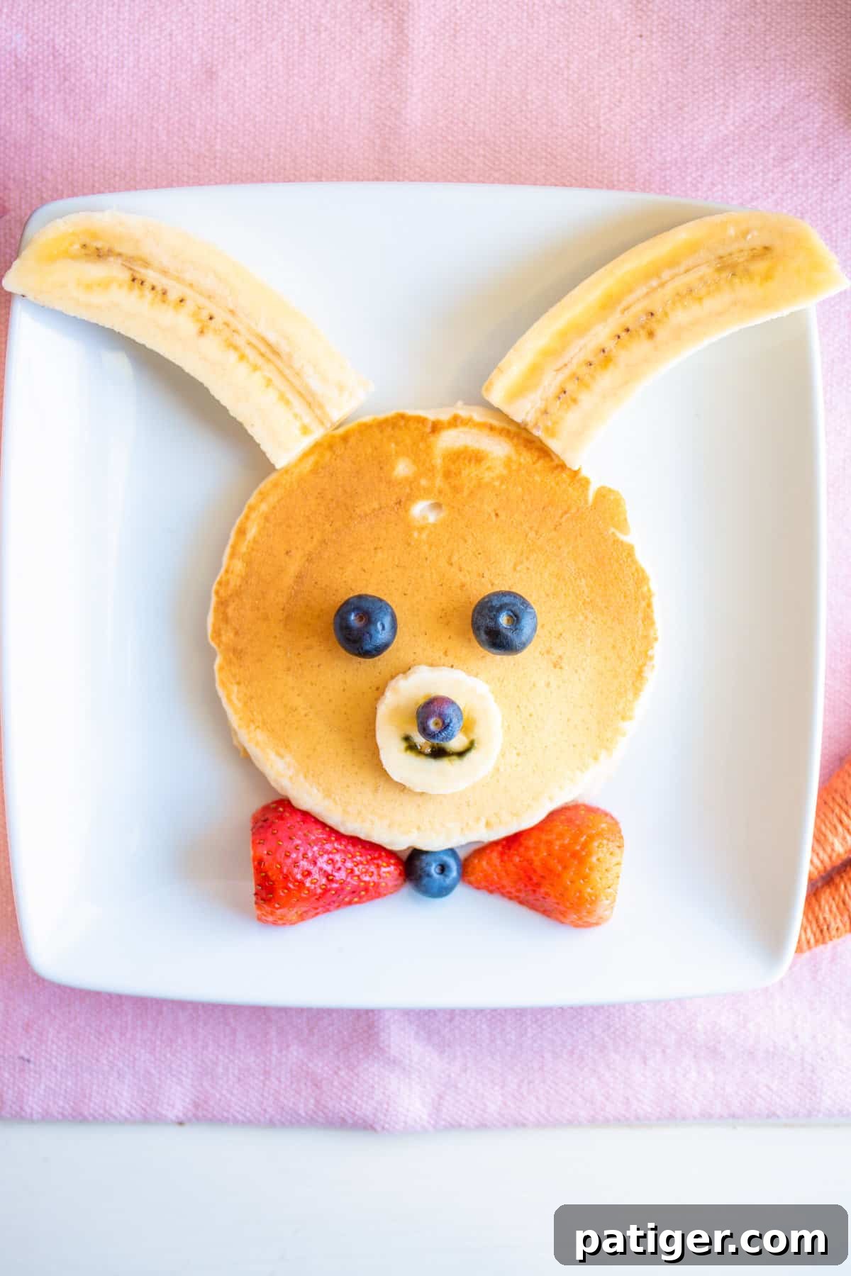 Bunny pancakes made with a large pancake and decorated with banana, strawberry, and blueberries, a festive breakfast.