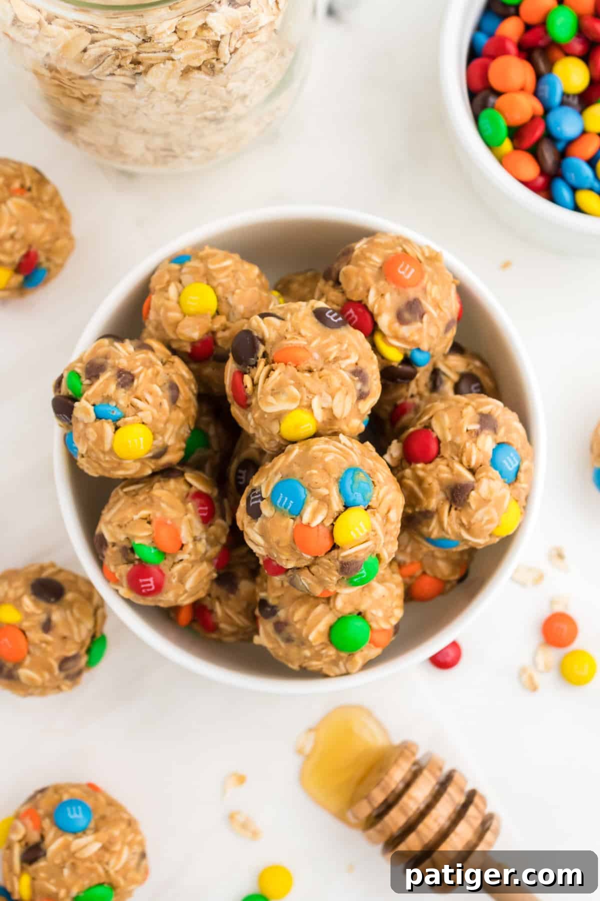 No-Bake Monster Cookie Energy Bites 9 Bowl of Oatmeal Balls with M&Ms surrounded by jar of oats, honey, M&M candies, and more energy balls.