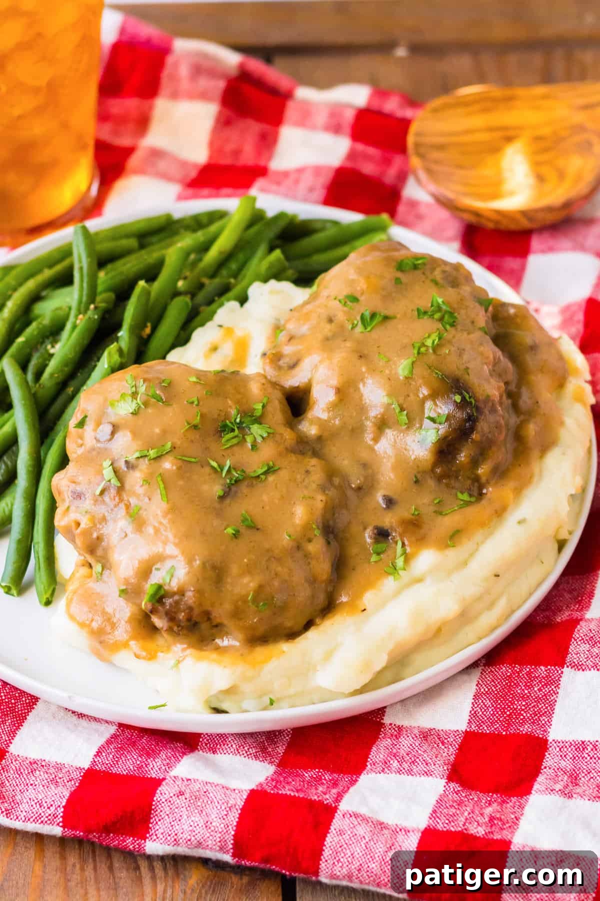 Tender Slow Cooker Salisbury Steaks 2 Slow cooker salisbury steaks smothered with brown gravy over a bed of mashed potatoes and served with a side of string beans.