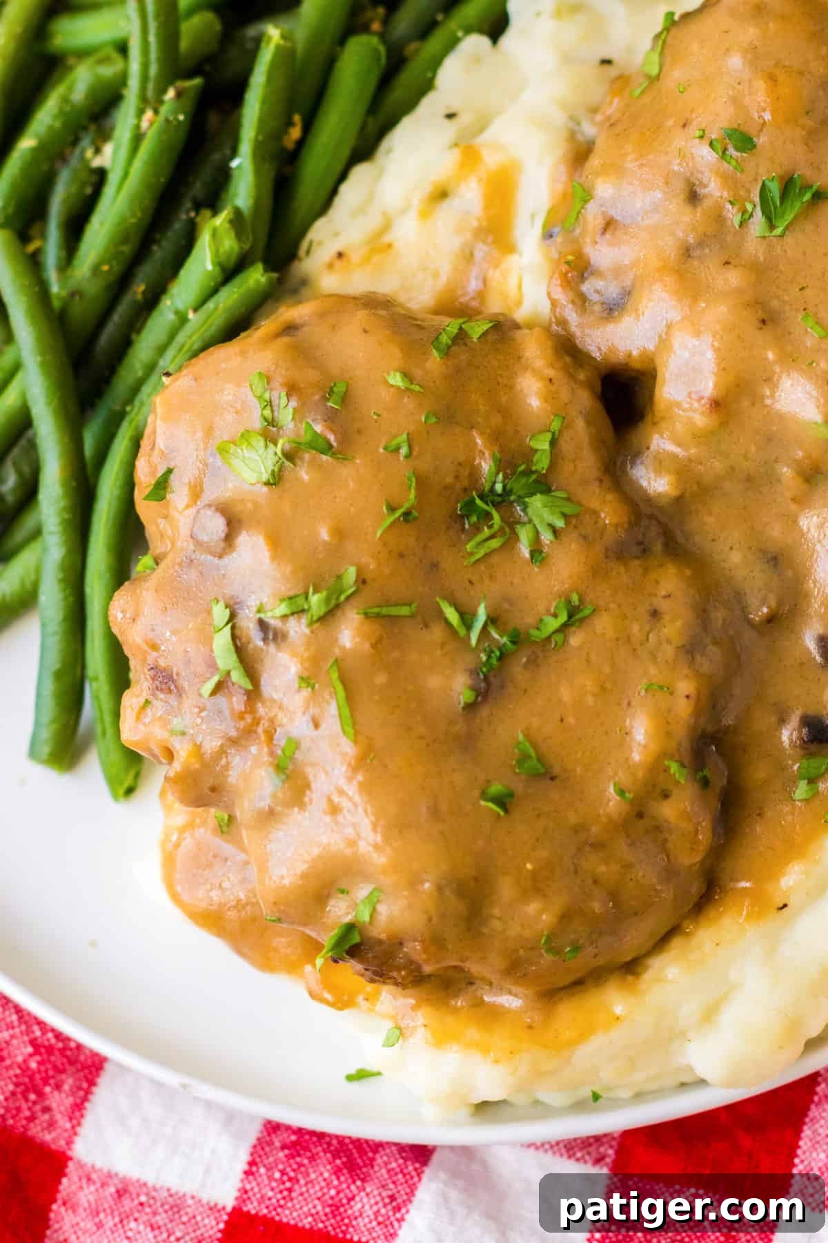 Tender Slow Cooker Salisbury Steaks 9 Crockpot salisbury steak with gravy served on a bed of mashed potatoes and garnished with chopped fresh parsley.