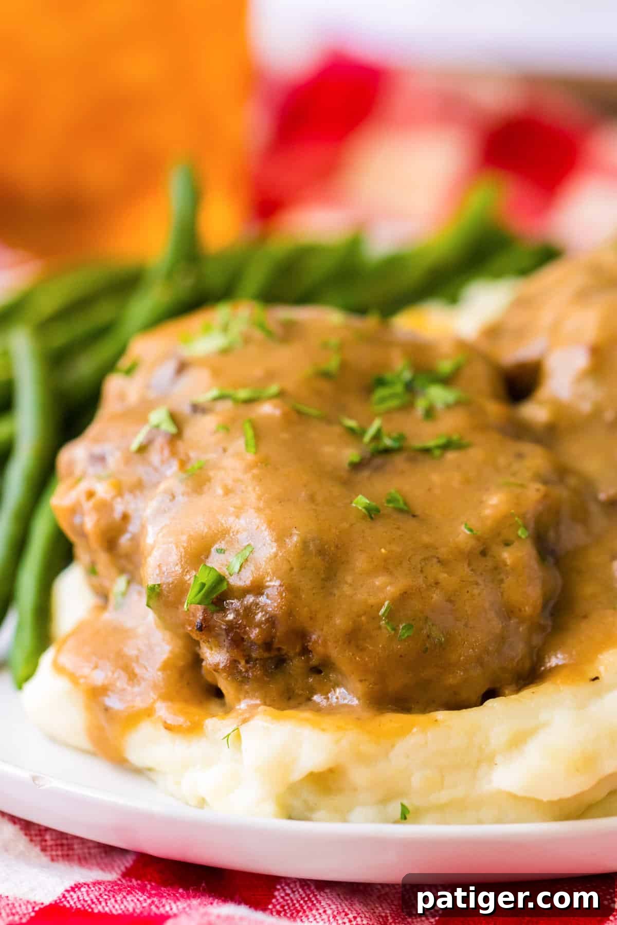 Tender Slow Cooker Salisbury Steaks 10 Side view of thick hamburger steak sitting on a bed of mashed potatoes and covered with brown gravy.