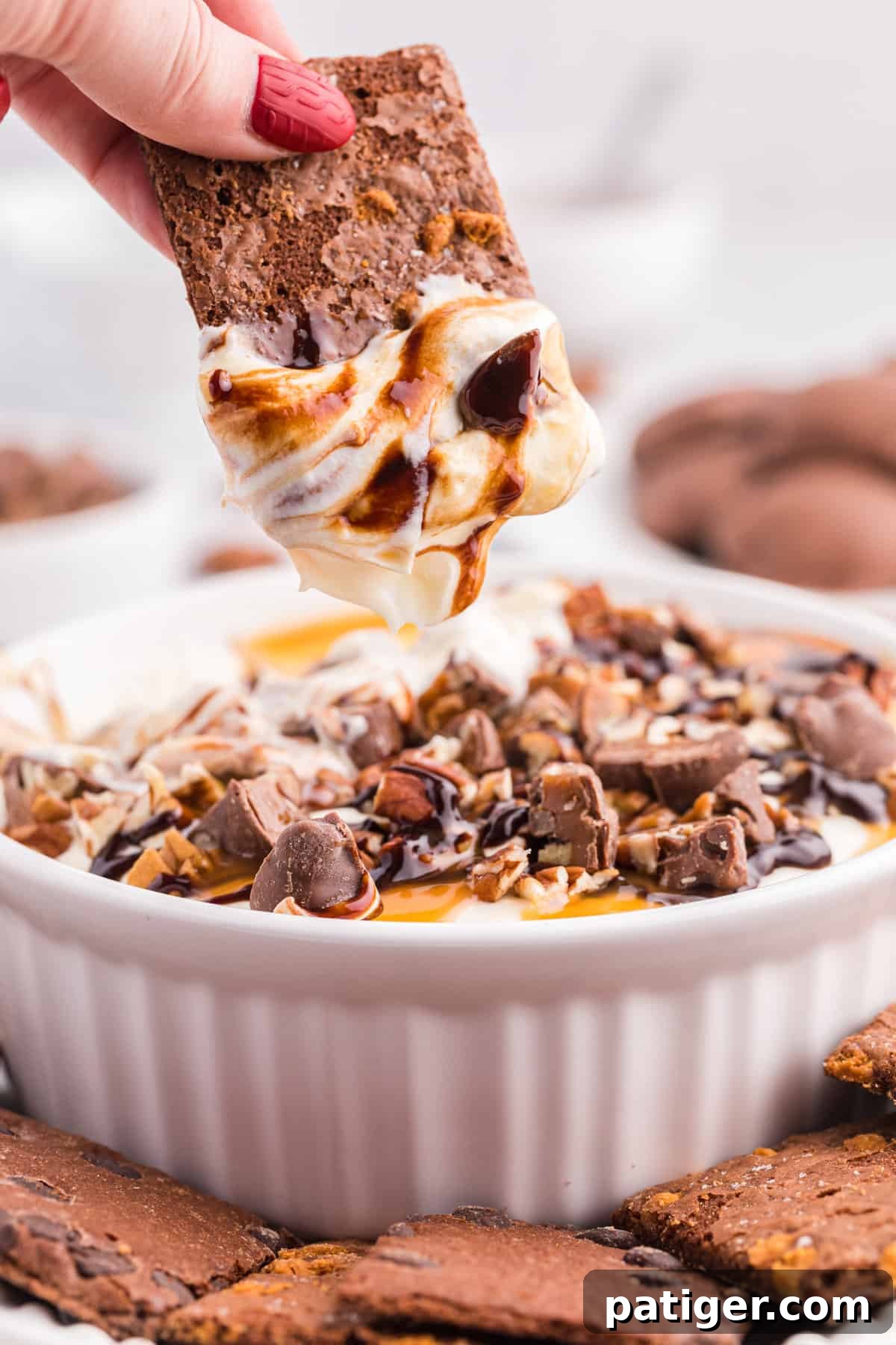 Hand reaching in to dip a chocolate cookie into the creamy no bake turtle cheesecake dip.
