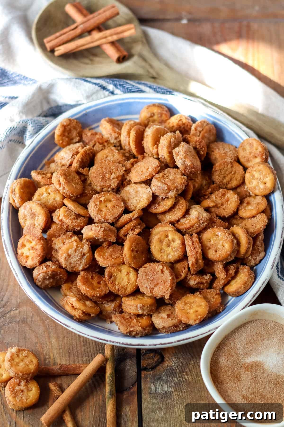 Ritz Cinnamon Churro Bites 2 Cinnamon sugar Ritz Churro Bites in a large serving bowl on a wooden table with a small bowl of cinnamon sugar and cinnamon sticks around it.