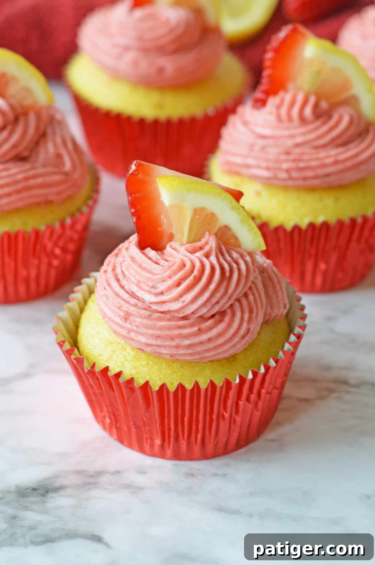 Pink Lemonade Swirl Cupcakes 2 Strawberry lemonade cupcakes garnished with fresh lemon slices and whole strawberries, showcasing their vibrant colors and appealing presentation.