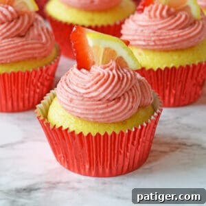 Pink Lemonade Swirl Cupcakes 8 Strawberry lemonade cupcakes topped with fresh lemon and strawberries, a perfect close-up for a recipe card.