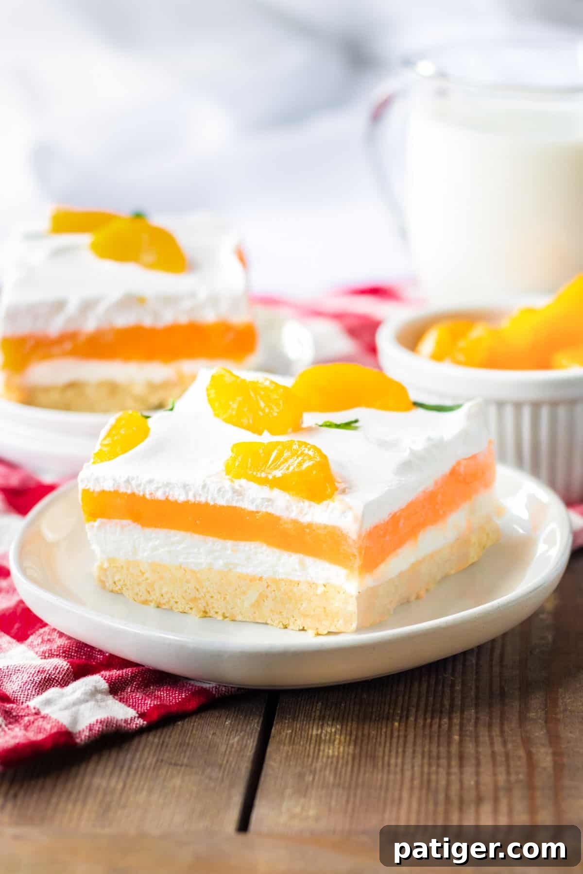 Orange creamsicle lush with layers of creamy vanilla pudding and orange jello, sweetened cream cheese, and cool whip on a sweet cookie crust. Mandarin orange pieces top the no bake cake.