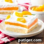 Orange creamsicle lush with layers of creamy vanilla pudding and orange jello, sweetened cream cheese, and cool whip on a sweet cookie crust. Mandarin orange pieces top the no bake cake.