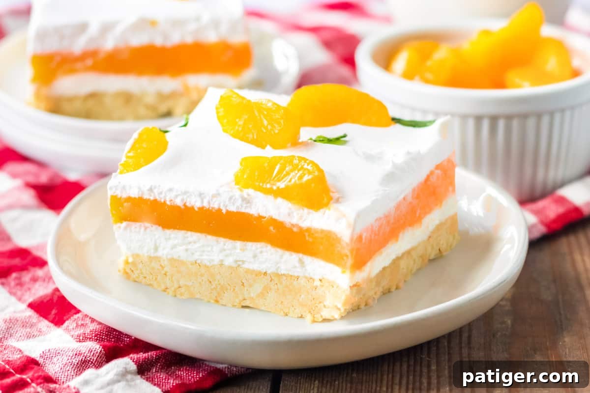 Orange creamsicle lush with layers of creamy vanilla pudding and orange jello, sweetened cream cheese, and cool whip on a sweet cookie crust. Mandarin orange pieces top the no bake cake.