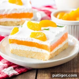 Orange creamsicle lush with layers of creamy vanilla pudding and orange jello, sweetened cream cheese, and cool whip on a sweet cookie crust. Mandarin orange pieces top the no bake cake.