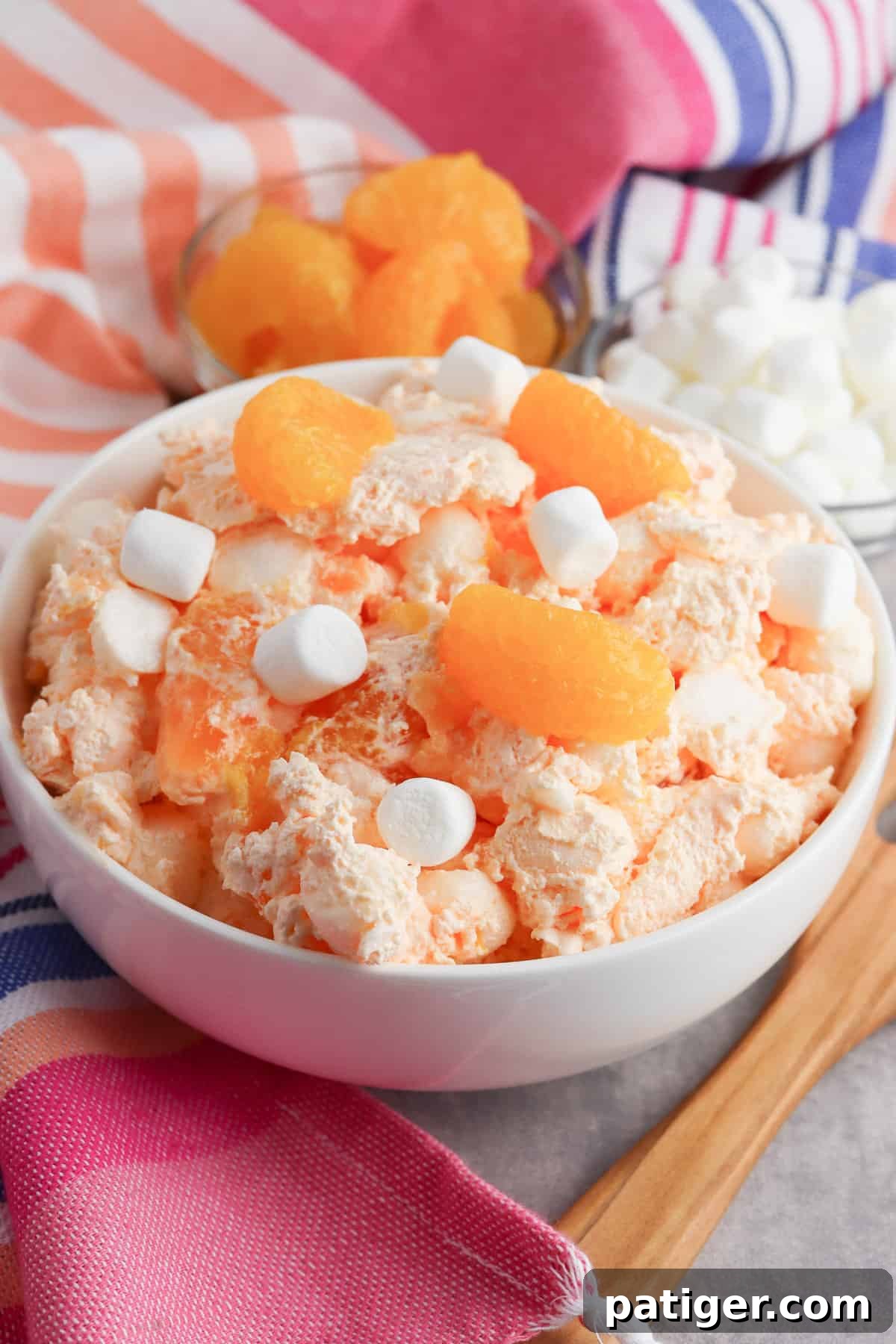 A vibrant bowl of Orange Fluff Salad, garnished with mini marshmallows and segments of mandarin oranges, ready to be served. 