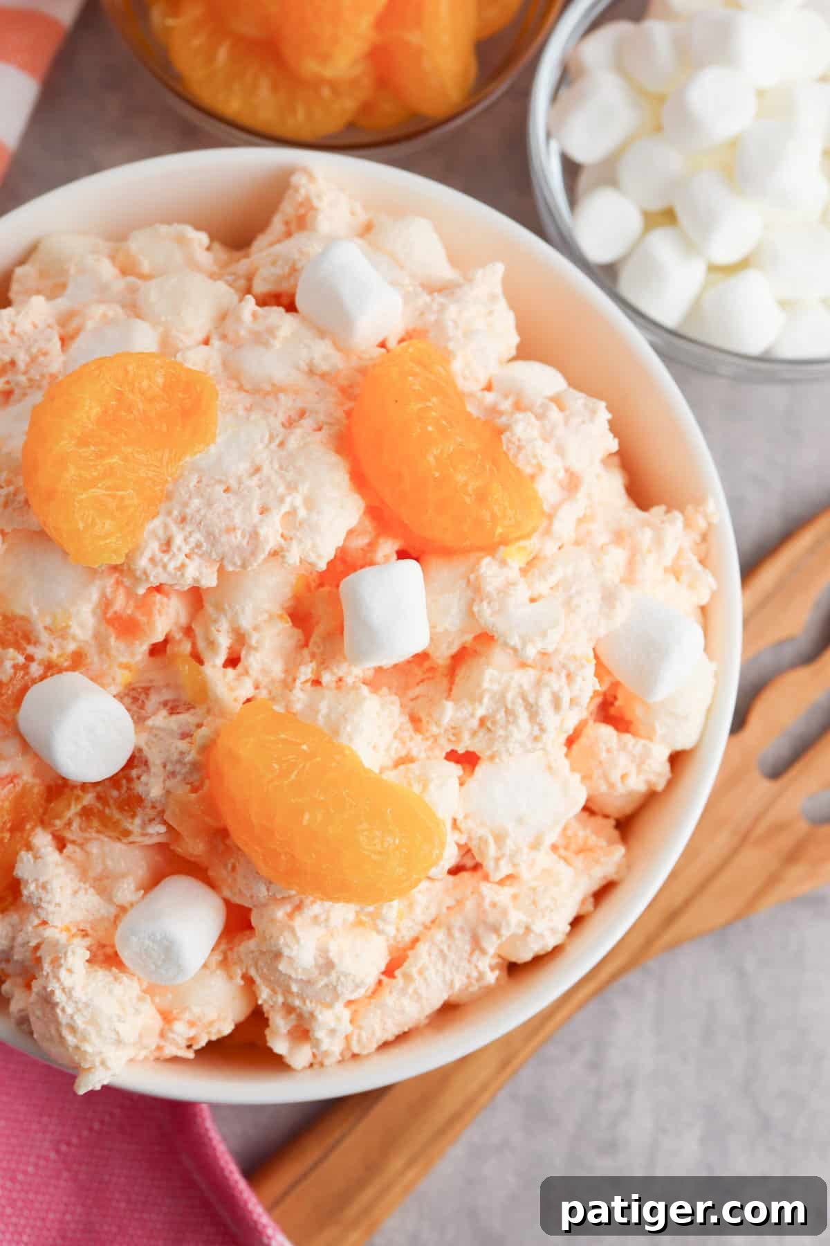 A large serving bowl filled with fluffy orange jello salad, mixed with mandarin oranges and mini marshmallows, highlighting its light and airy texture.