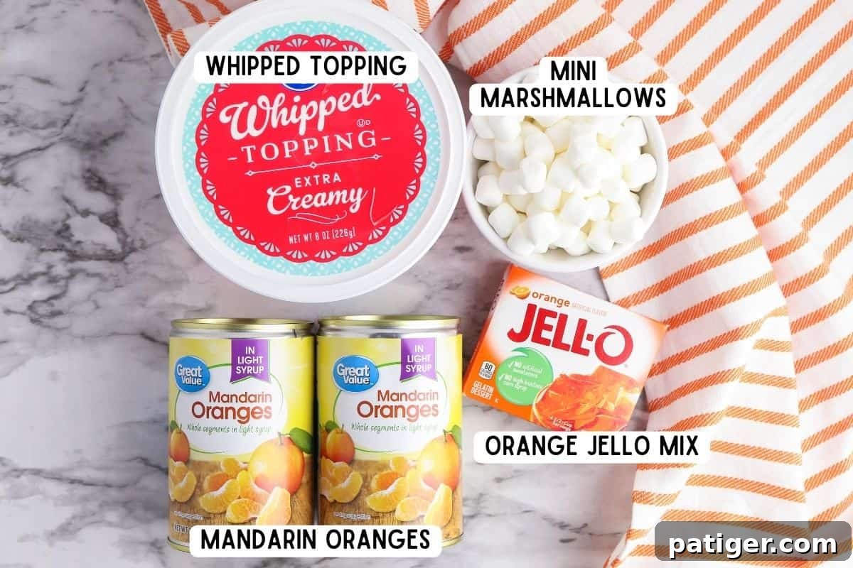 The essential ingredients for Orange Fluff: two cans of mandarin oranges, a box of orange Jell-O mix, a bowl of mini marshmallows, and a container of whipped topping.