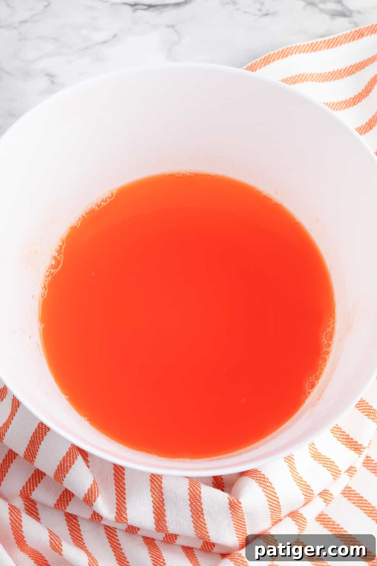 Orange jello mixture in a clear mixing bowl, just after dissolving and cooling, ready for the next step.