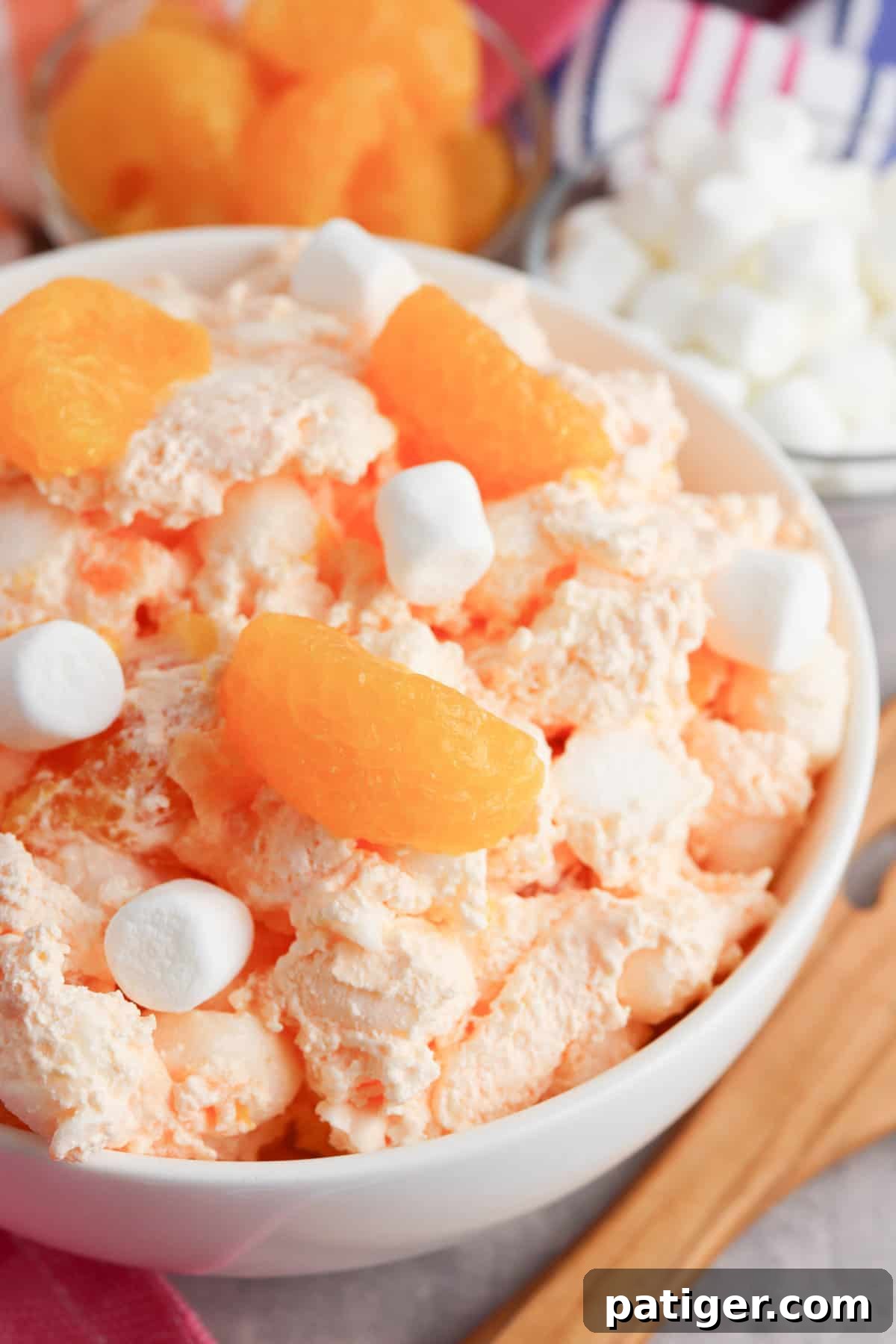 A large bowl of finished Orange Creamsicle Salad, ready to be served with a wooden serving spoon.
