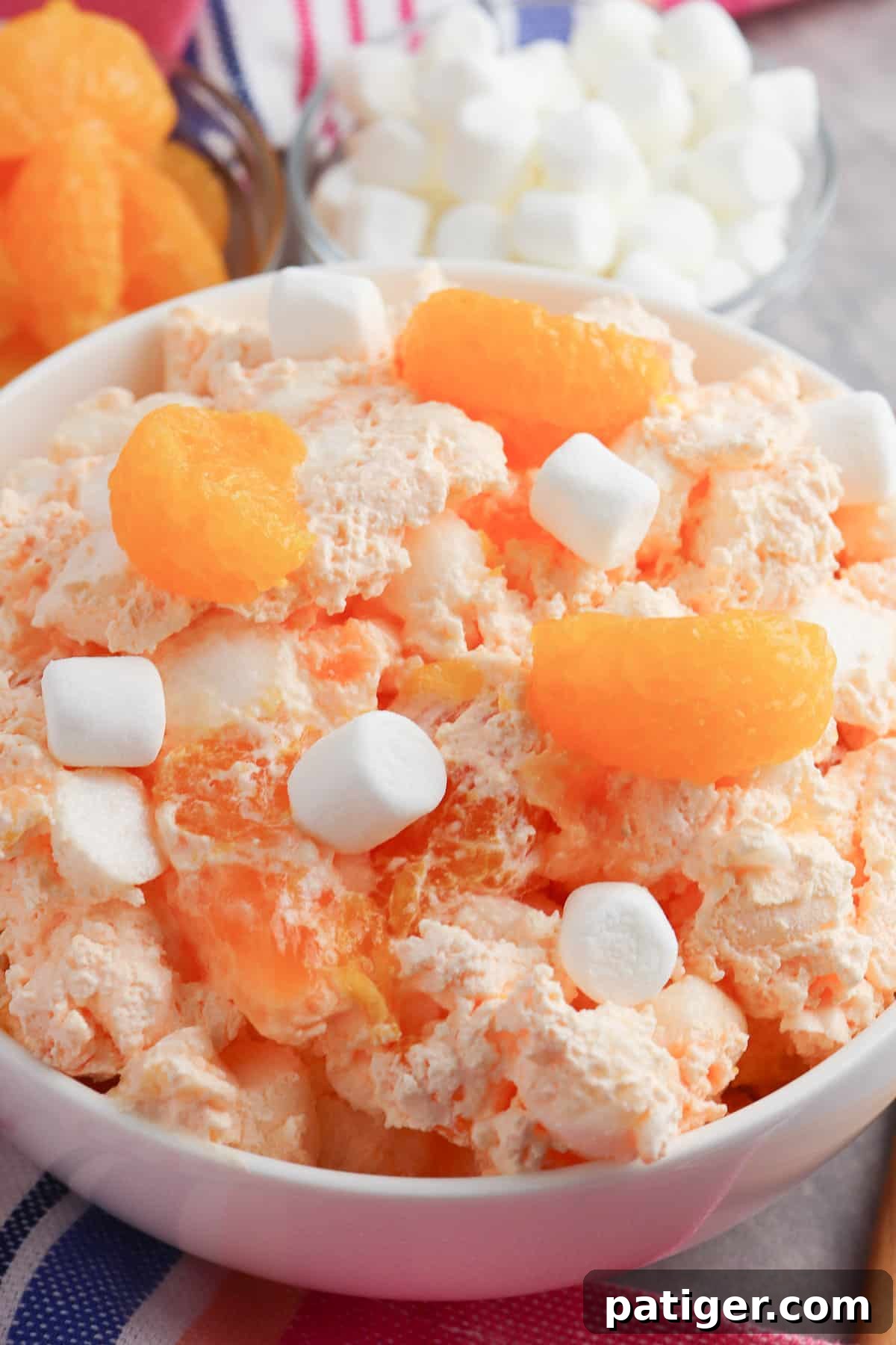 A close-up of a bowl of mandarin orange jello salad, adorned with additional marshmallows, highlighting its inviting texture and bright color.