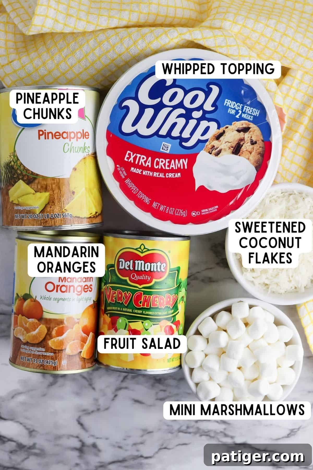 Cloud Nine Fruit Salad 4 Ingredients for marshmallow fruit salad: cool whip, shredded coconut, mini marshmallows, and cans of fruit cocktail, mandarin oranges, and pineapple chunks.