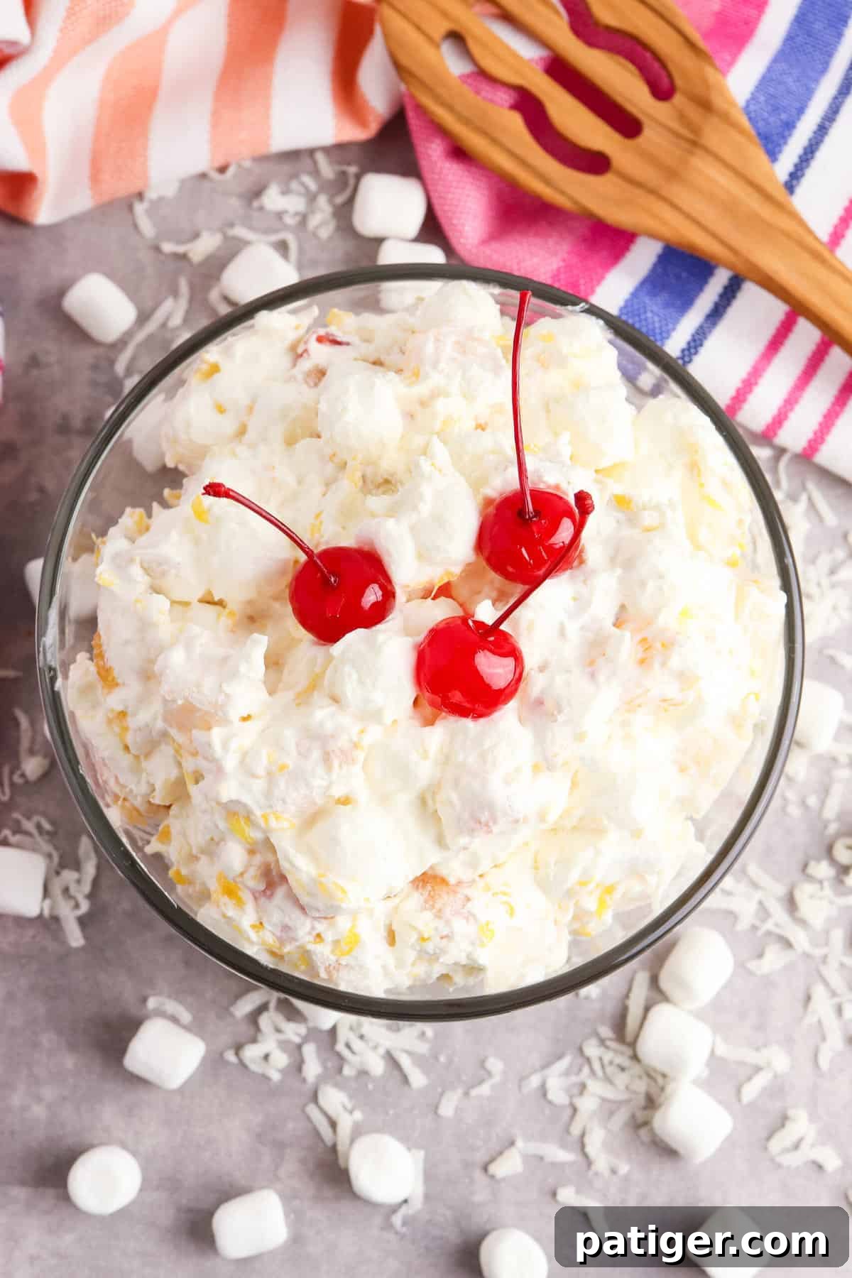 Cloud Nine Fruit Salad 7 Overhead shot of the finished fluffy marshmallow fruit salad in a white serving bowl, surrounded by scattered coconut flakes and mini marshmallows.