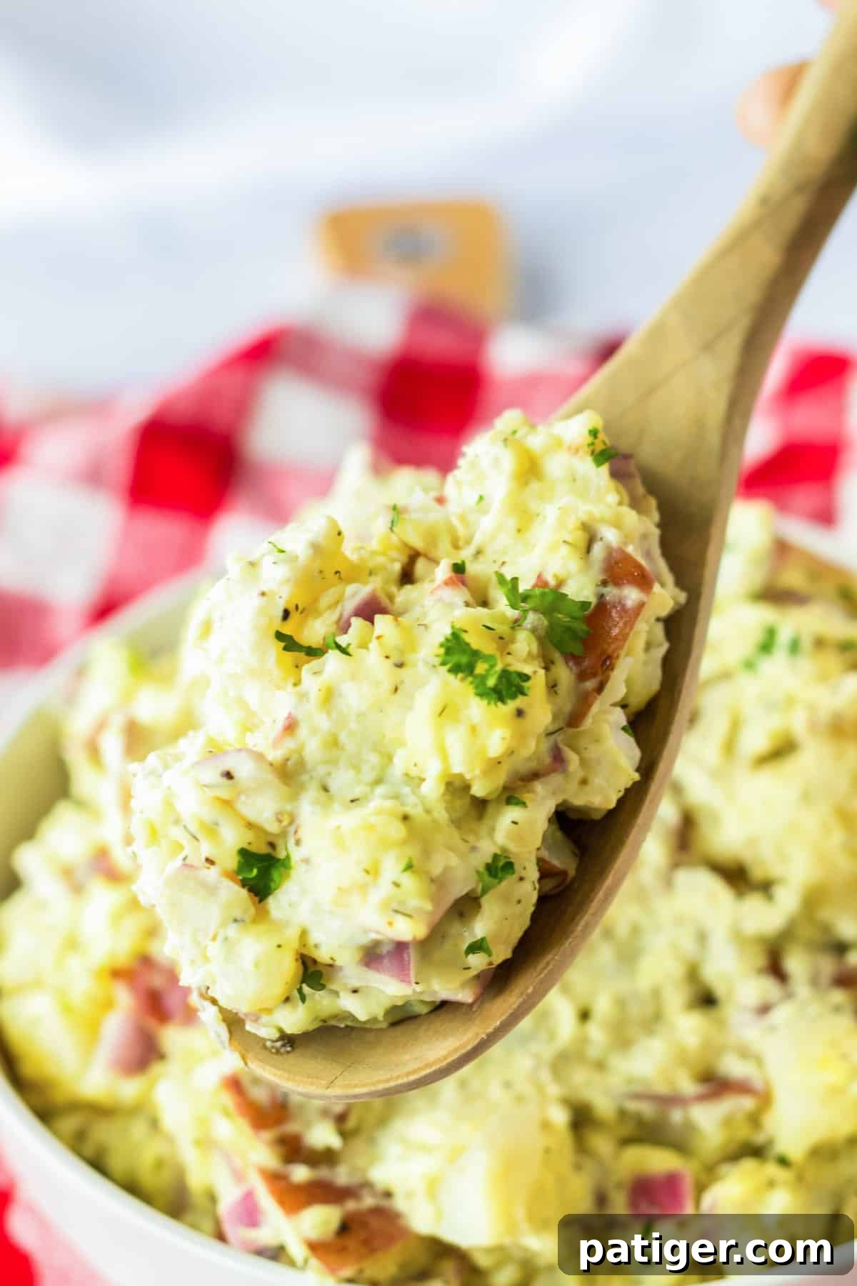 Red skin potato salad in a wooden spoon being lifted from bowl.