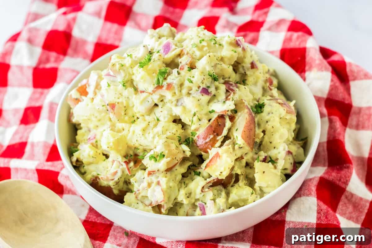 Old-fashioned red skin potato salad in white bowl on red plaid linen.