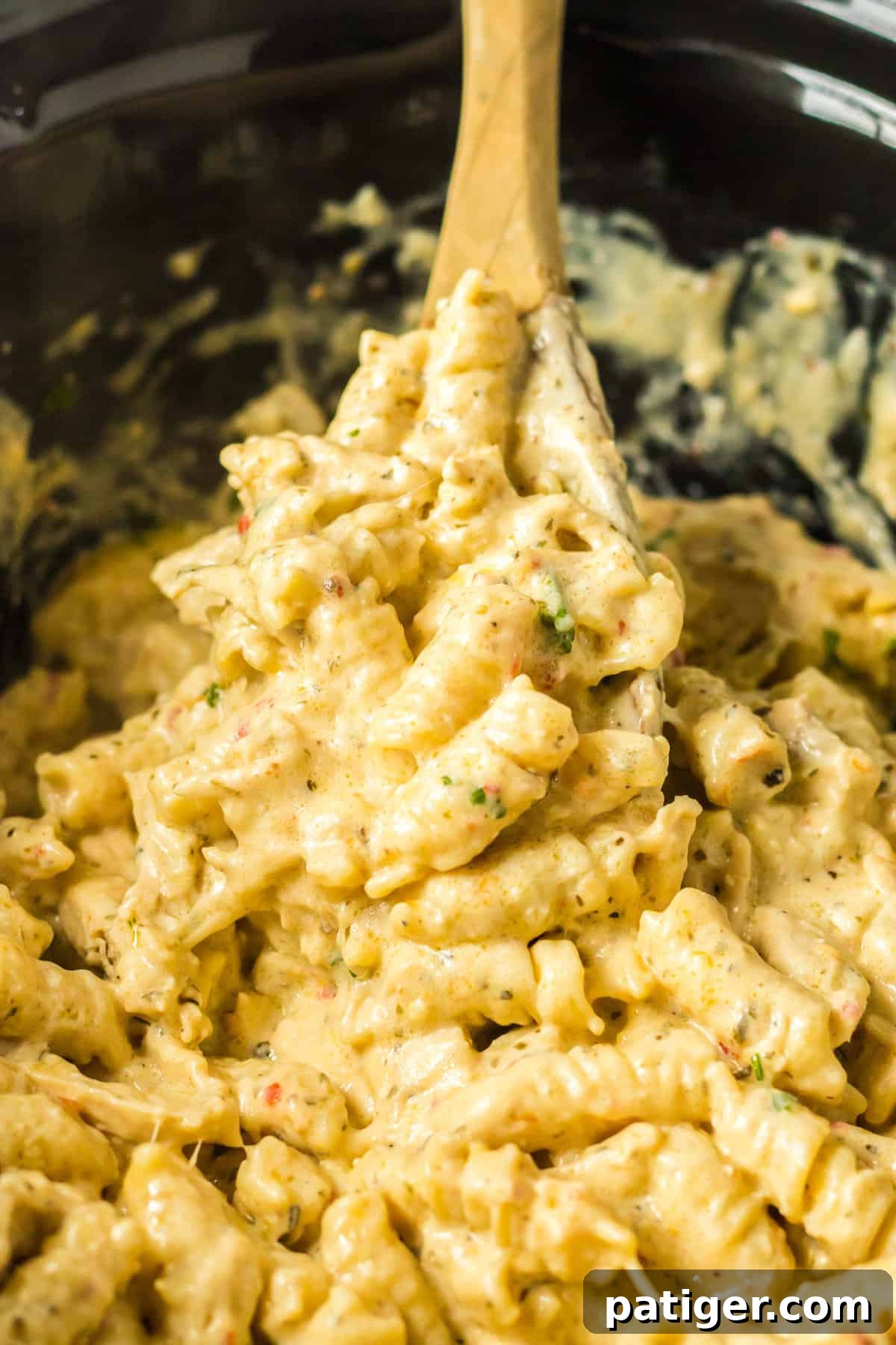 Creamy Crockpot Garlic Parmesan Chicken Pasta 2 Crockpot parmesan garlic chicken pasta in bowl of a slow cooker with a wooden spoon stirring it.