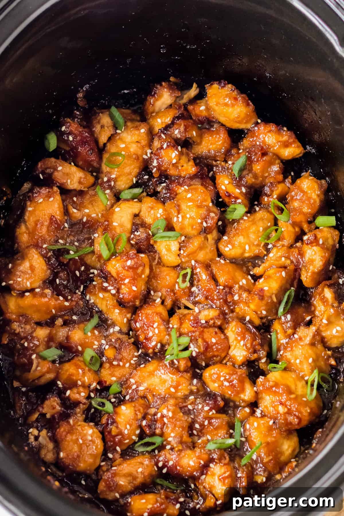 Orange chicken in the slow cooker garnished with sesame seeds and scallions.