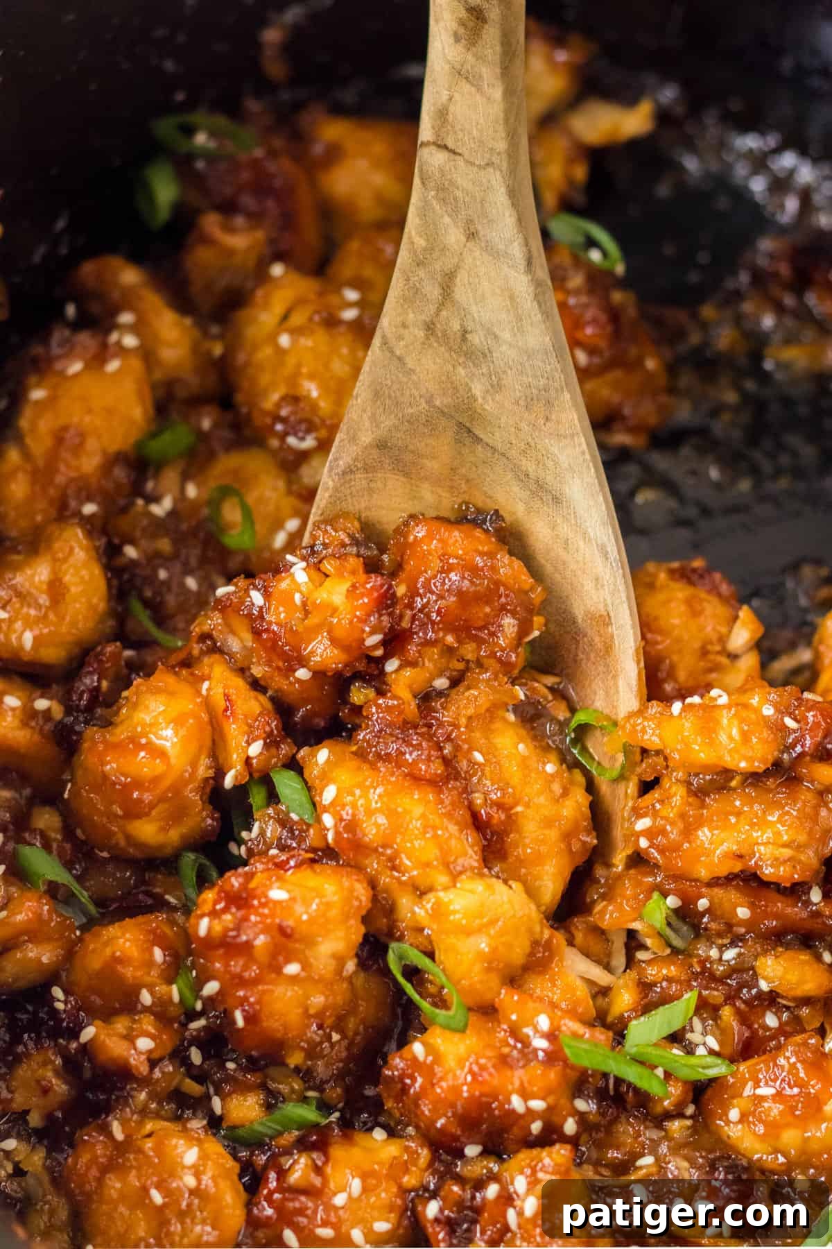 Wooden spoon stirring orange chicken in crock pot.