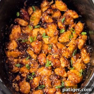 Slow Cooker orange chicken in bowl of a crockpot topped with sesame seeds and scallions.