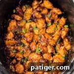 Slow Cooker orange chicken in bowl of a crockpot topped with sesame seeds and scallions.