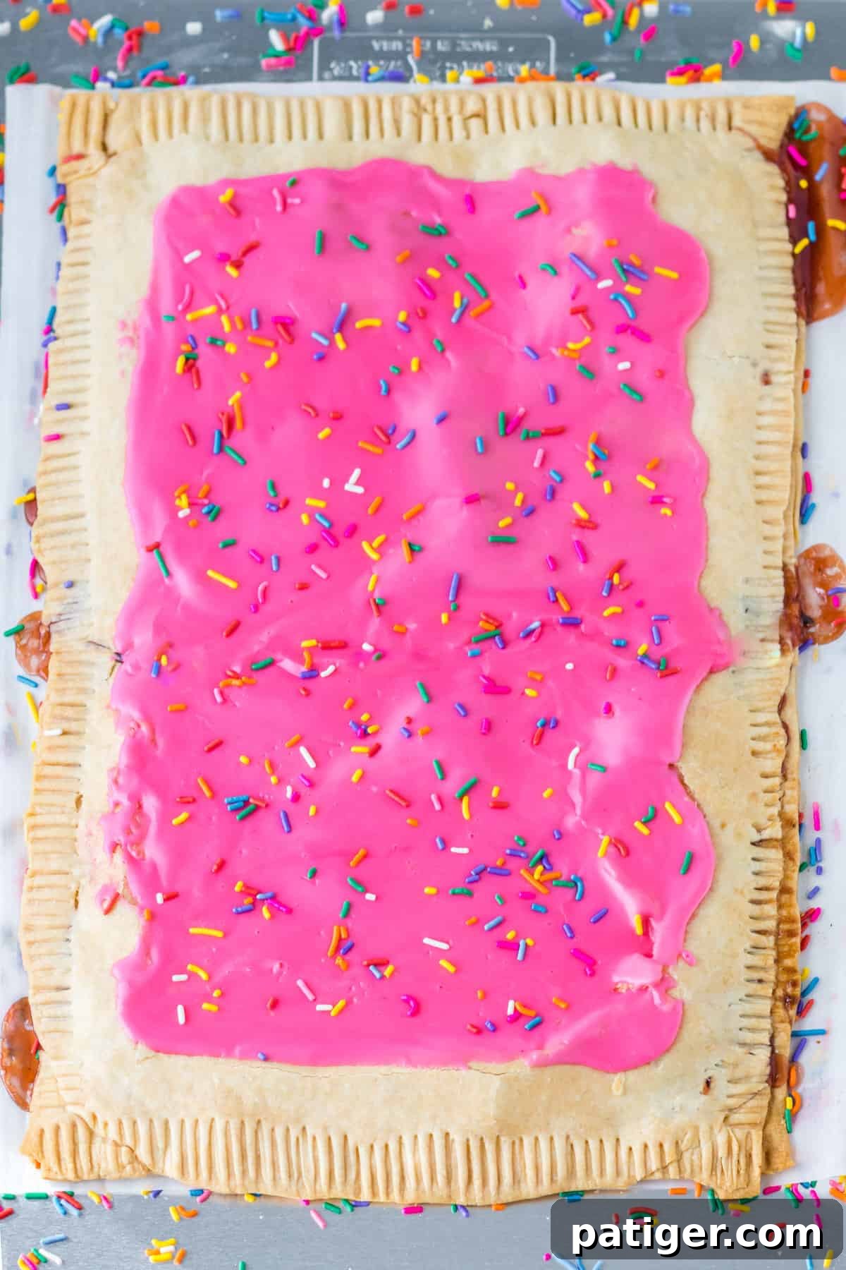 Giant strawberry pop tart with pink frosting and sprinkles on parchment lined sheet pan.