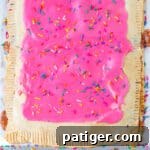 Giant strawberry pop tart with pink frosting and sprinkles on parchment lined sheet pan.