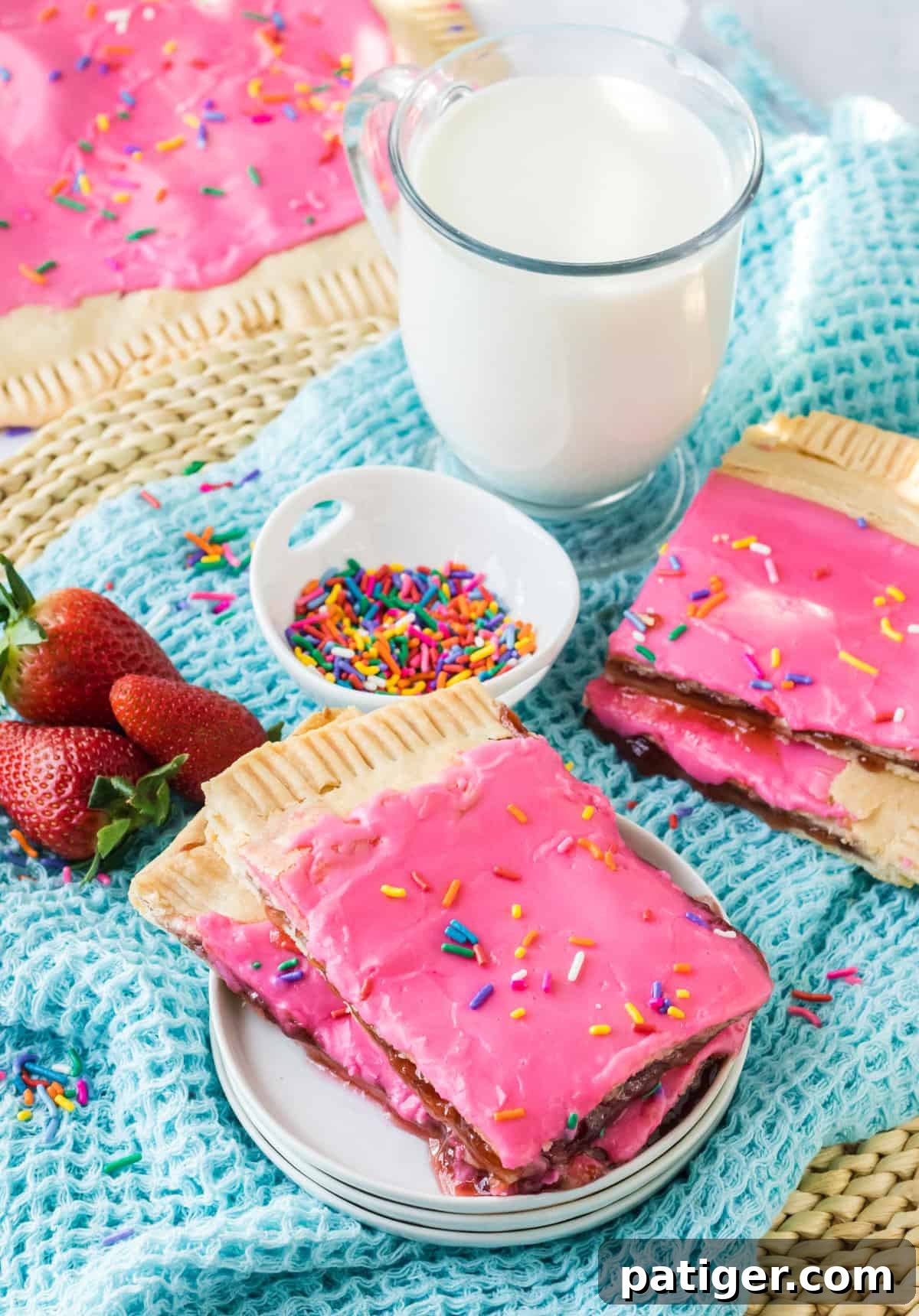Pieces of a homemade sheet pan pop tart on a plate with more pieces, glass of milk, and sprinkles in the background.