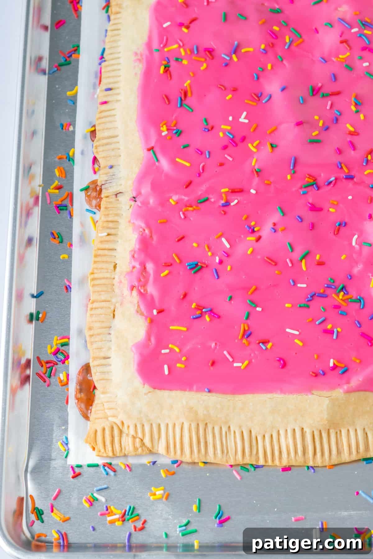 Homemade giant strawberry pop tart made with pie crust, strawberry jam, pink icing, and rainbow sprinkles on a sheet pan.