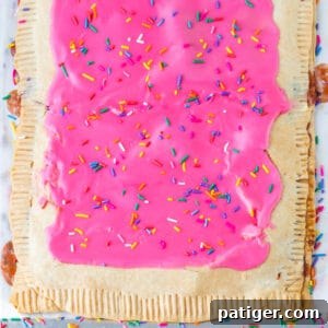 Giant strawberry pop tart with pink frosting and sprinkles on parchment lined sheet pan.