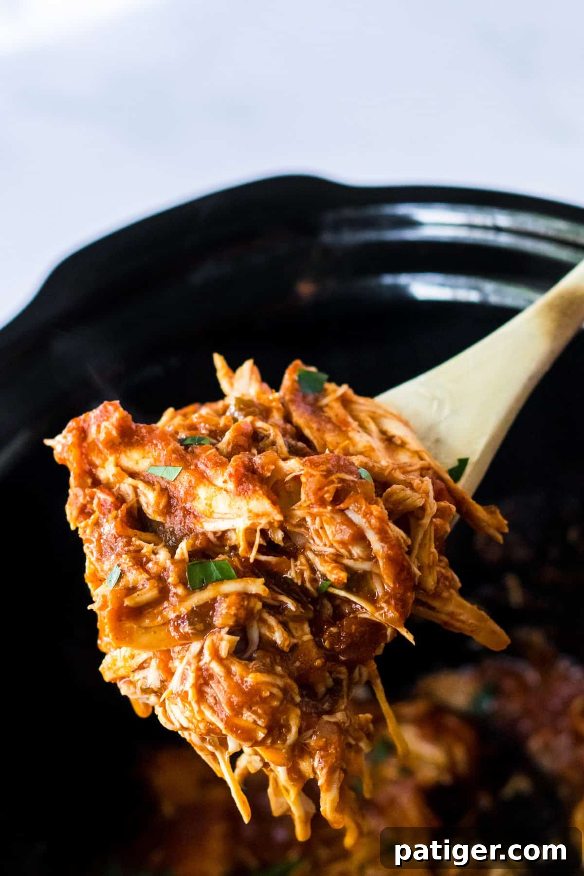 Shredded chicken breasts with salsa being scooped out of the slow cooker for serving.