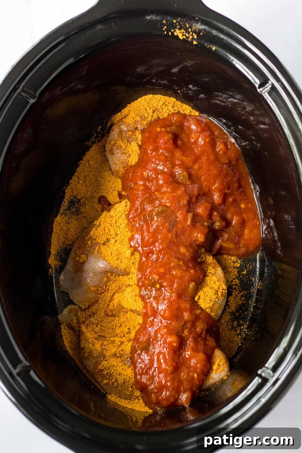 Chicken breasts arranged in a crockpot, ready to be seasoned and topped with salsa.