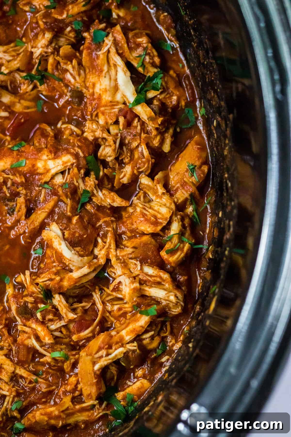 Close-up of slow cooker shredded chicken with taco seasoning and salsa, showcasing its texture and rich color.