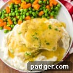 Pork chops smothered in gravy served over mashed potatoes and with a side of peas and carrots.