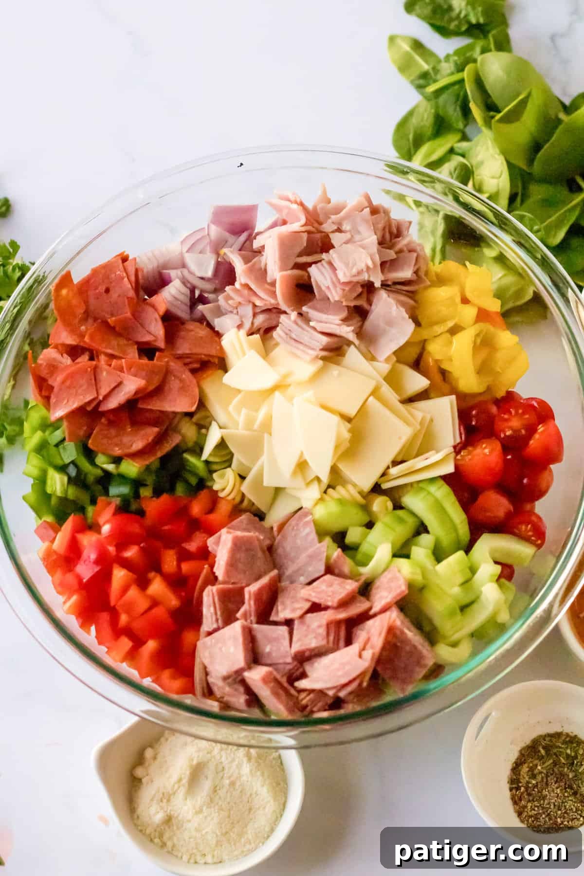 Italian Hoagie Pasta Salad 5 A clear glass bowl filled with meticulously chopped deli meat, cubed cheese, and a colorful array of fresh vegetables, ready for mixing.